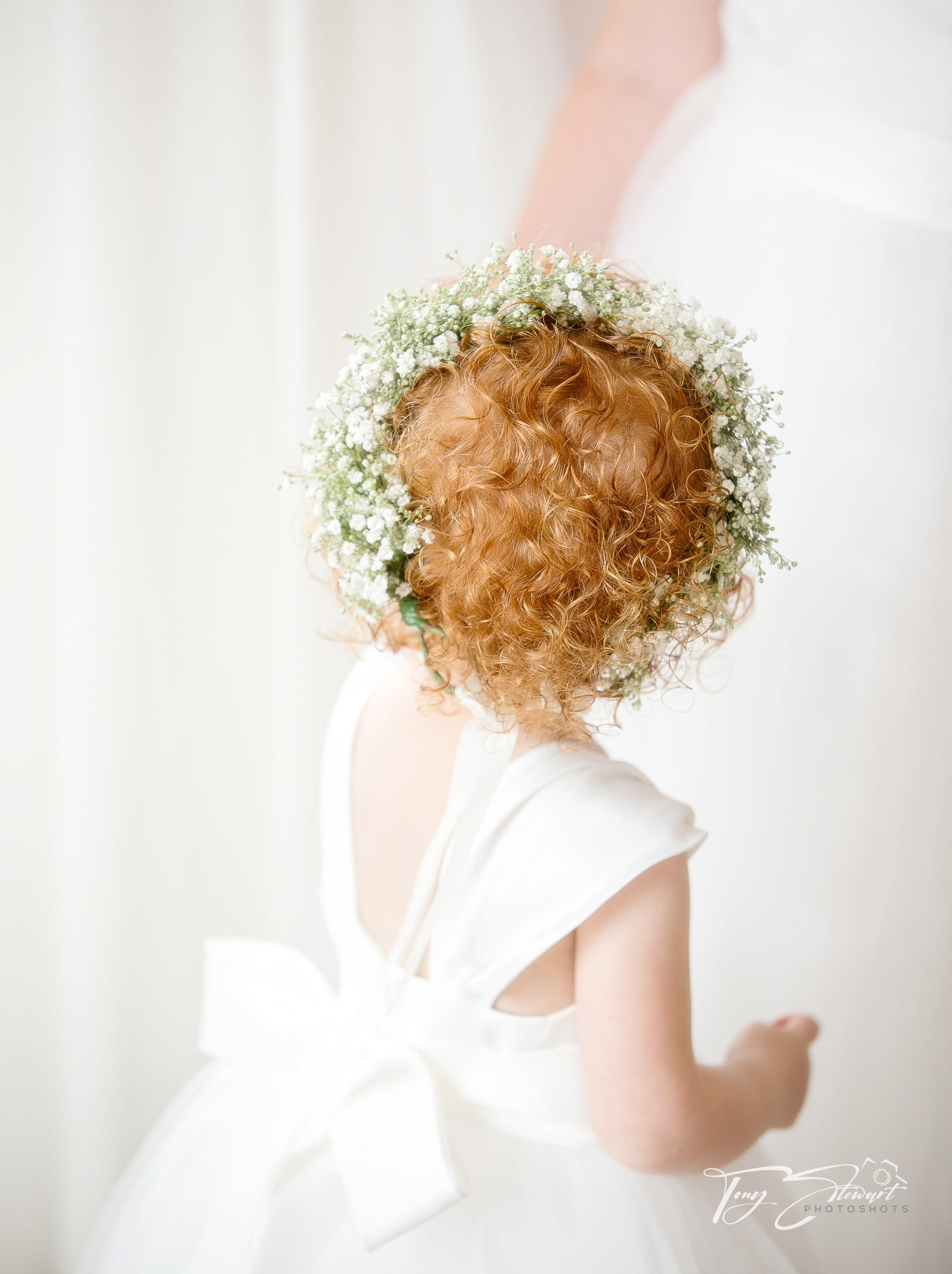 Ginger haired bridesmaid looks up to hanging bridal dress.