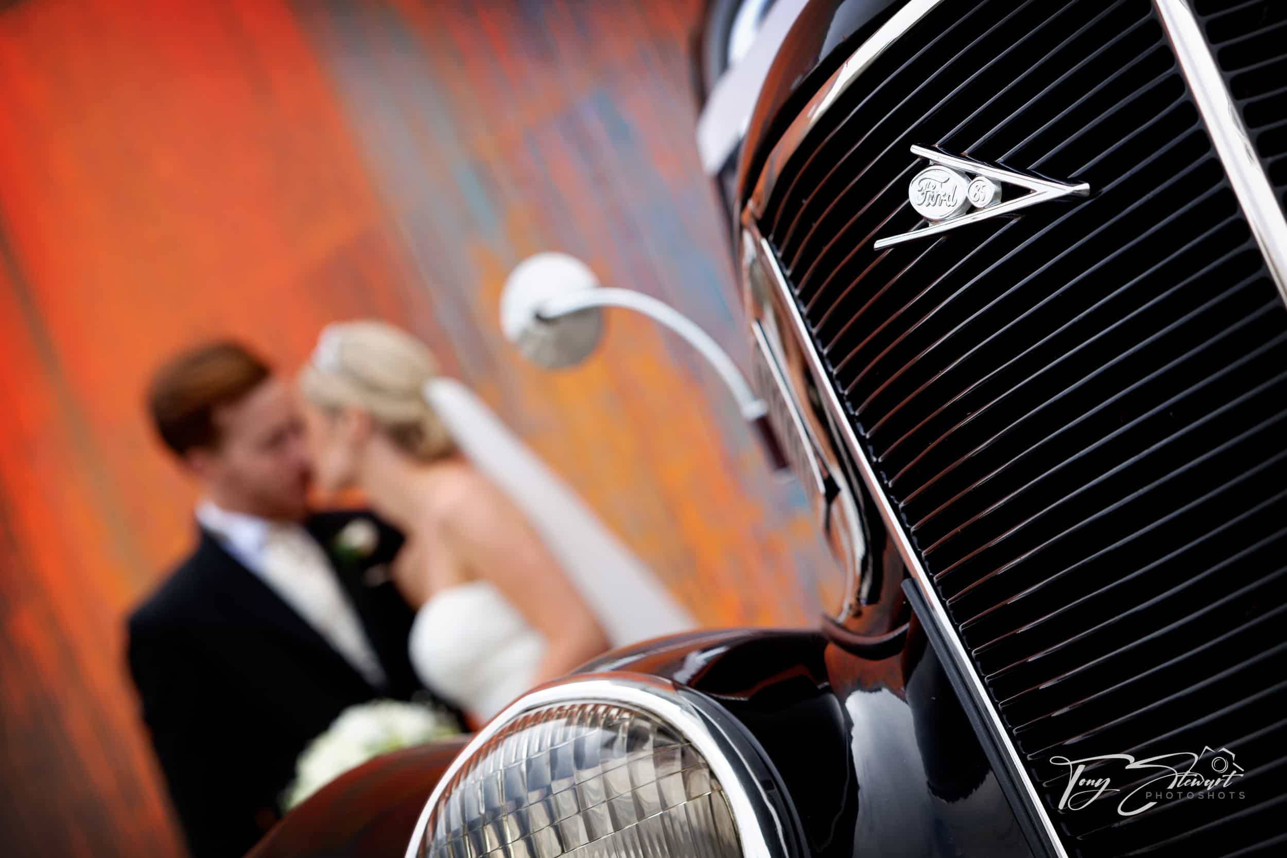 Wedding couple kiss at the rear of their vintage wedding car, Christchurch CBD.
