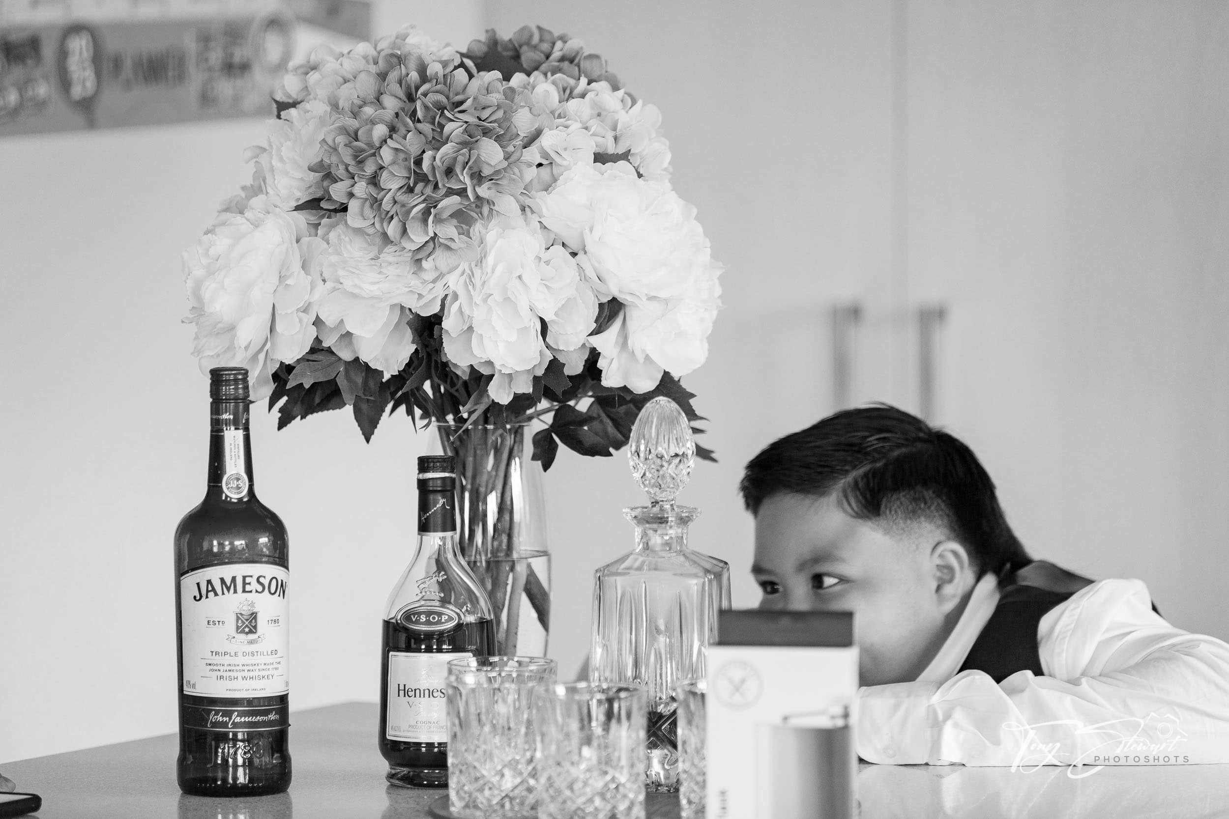 Young page boy eyes up whiskey on a kitchen bench before a wedding.