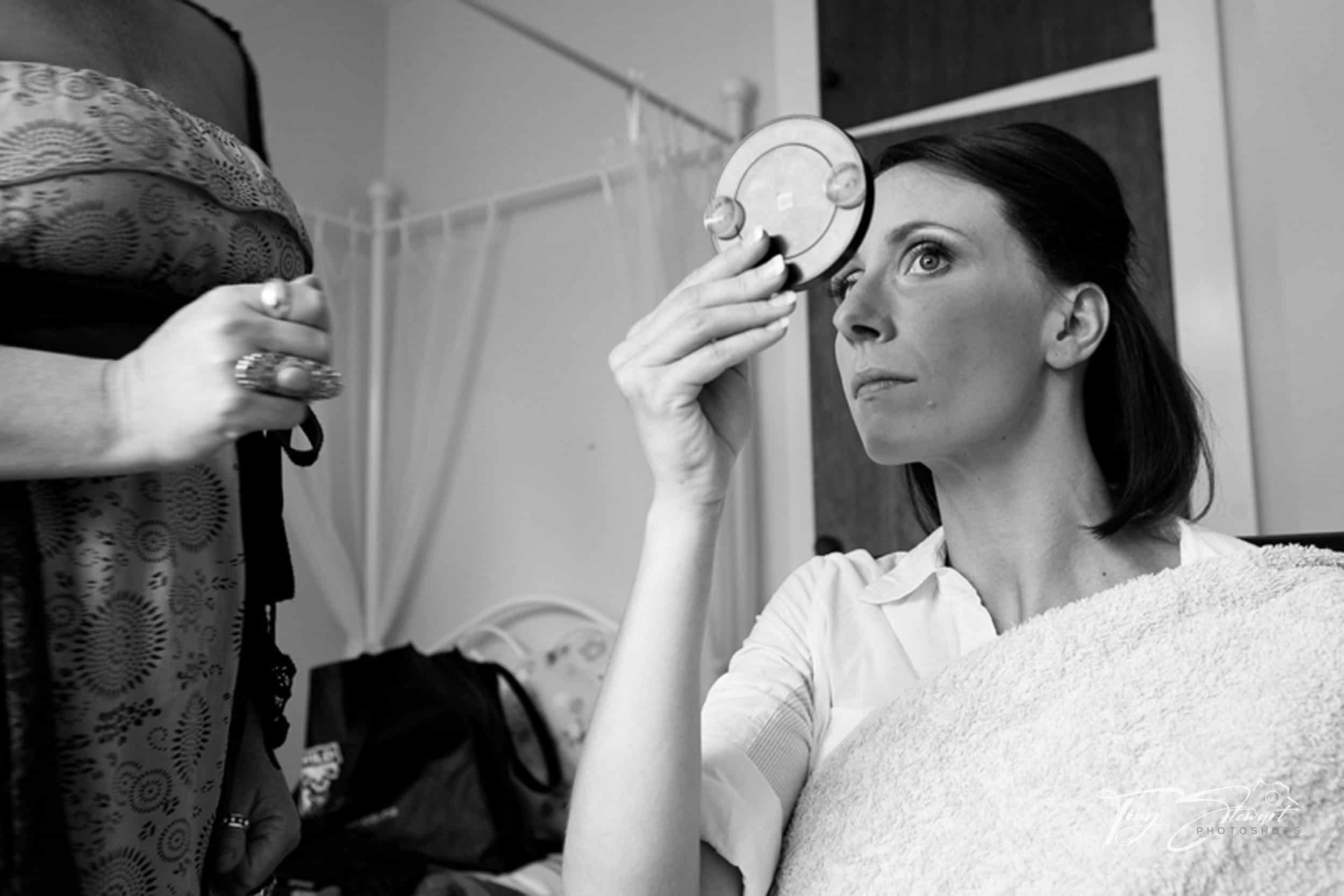 Bride checks her make up in a compact mirror before her wedding.