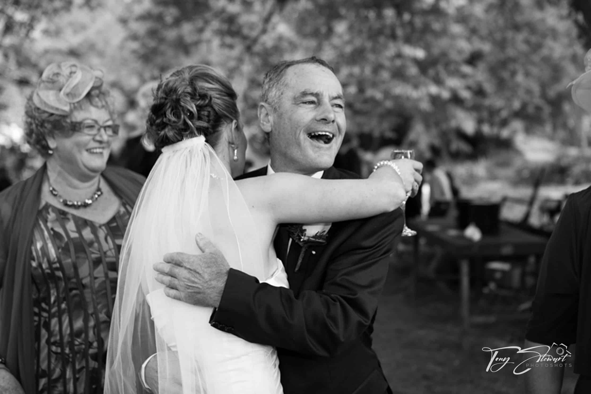 Dad laughs and hugs bride after her wedding ceremony.