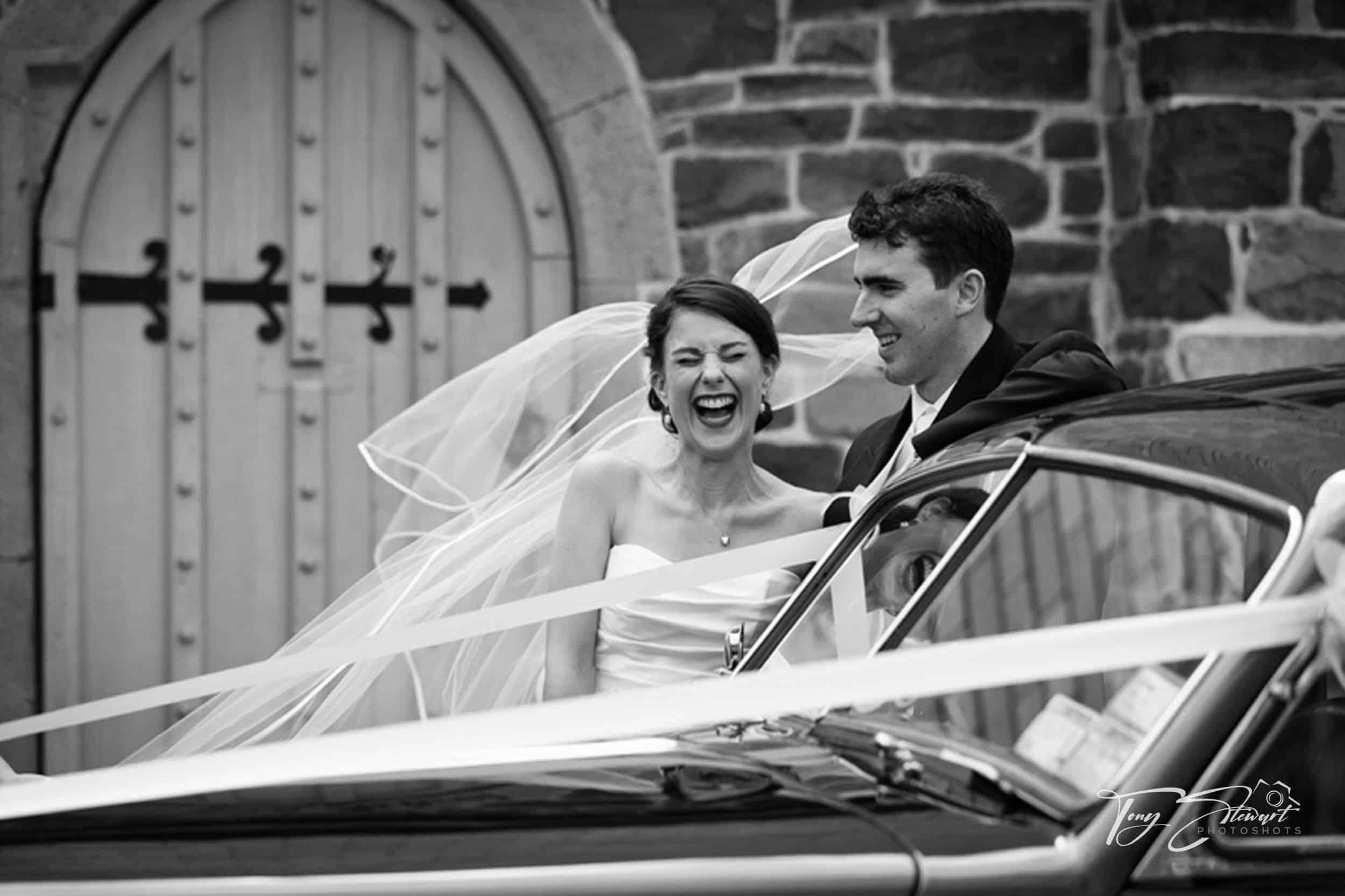 Excited couple share a tender moment standing by their vintage car outside St Pauls church after their wedding.