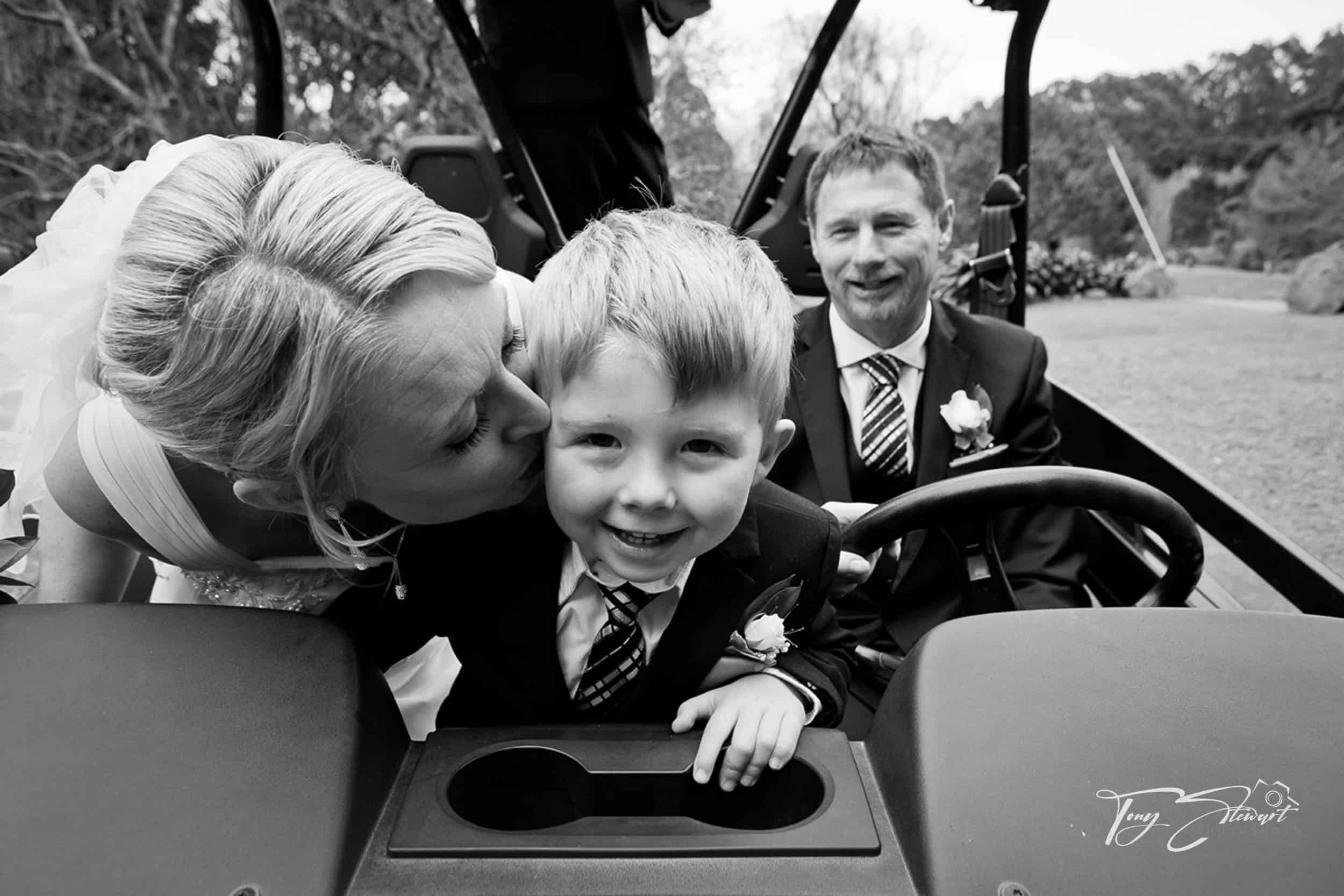 Son of bride gets kissed on cheek by his Mum, while his Dad drives a side by side at their wedding ceremony in Akaroa.