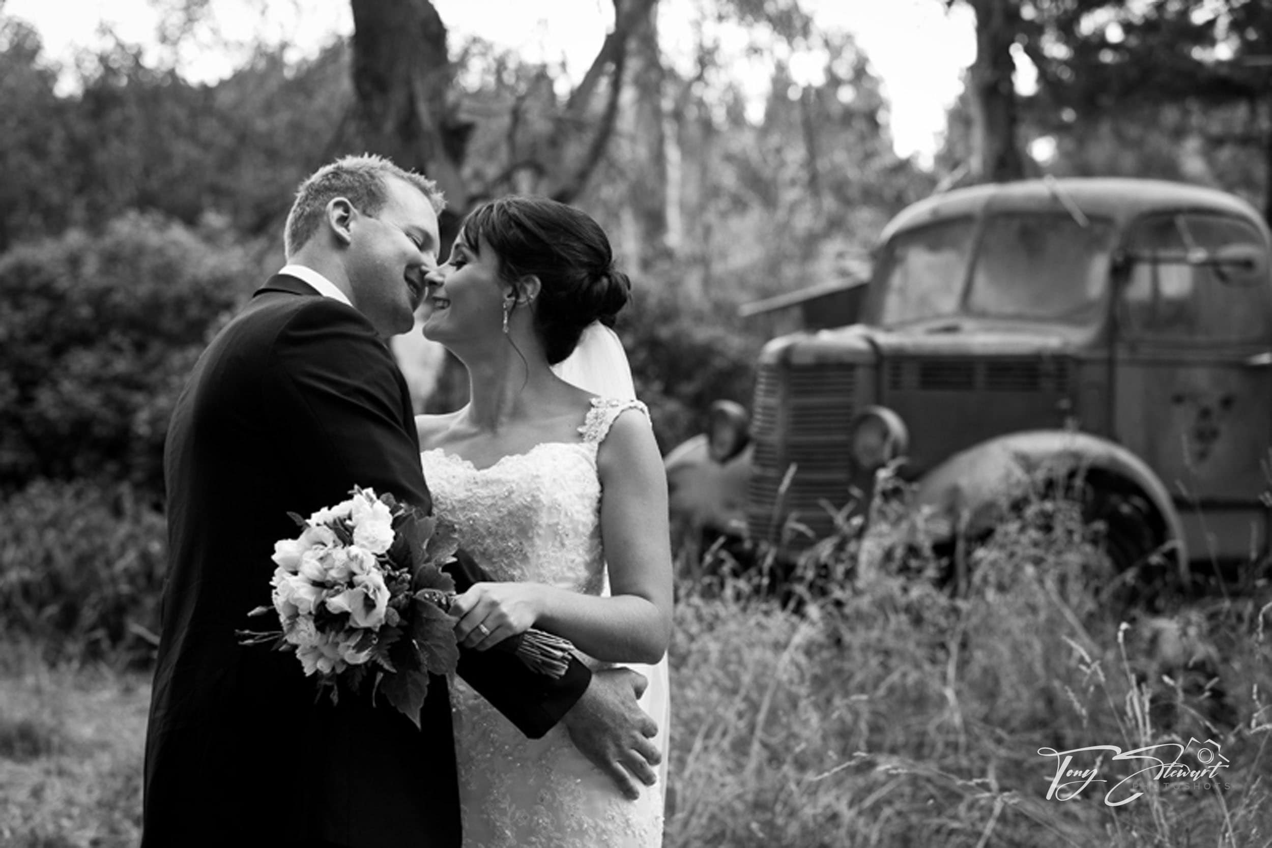 A newly wedded couple share a kiss in front of a rusted truck, at Trents Estate Vineyard.