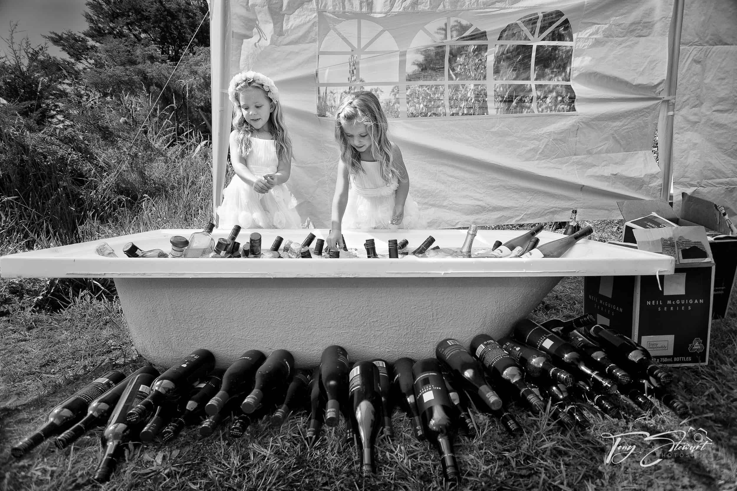 Two young bridesmaids look over bath full of chilled wine.