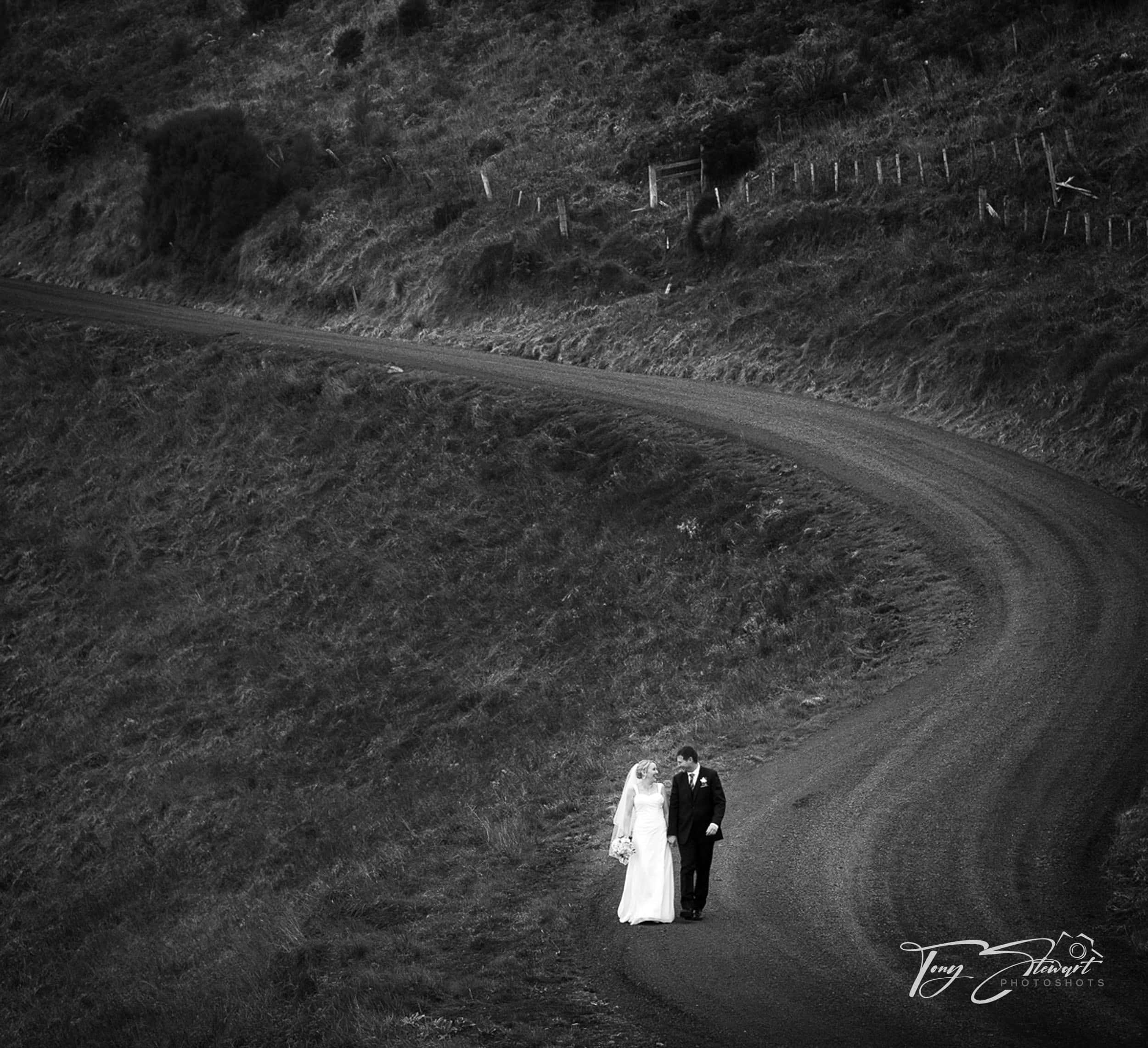 Bride and groom walk down winding road, Banks Peninsula.