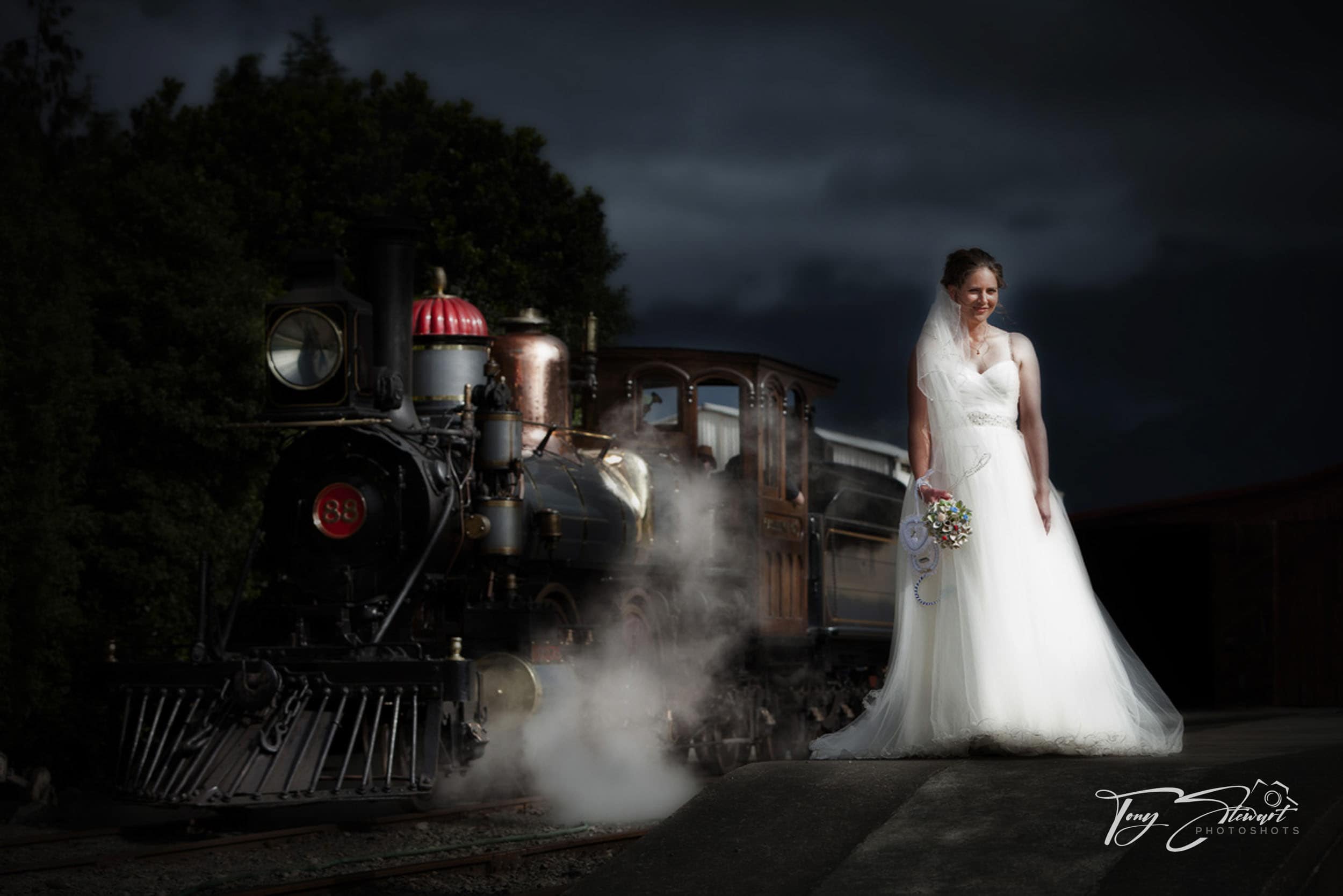 Bride stands amidst the steam of vintage train, at the Plains Railway, Tinwald.