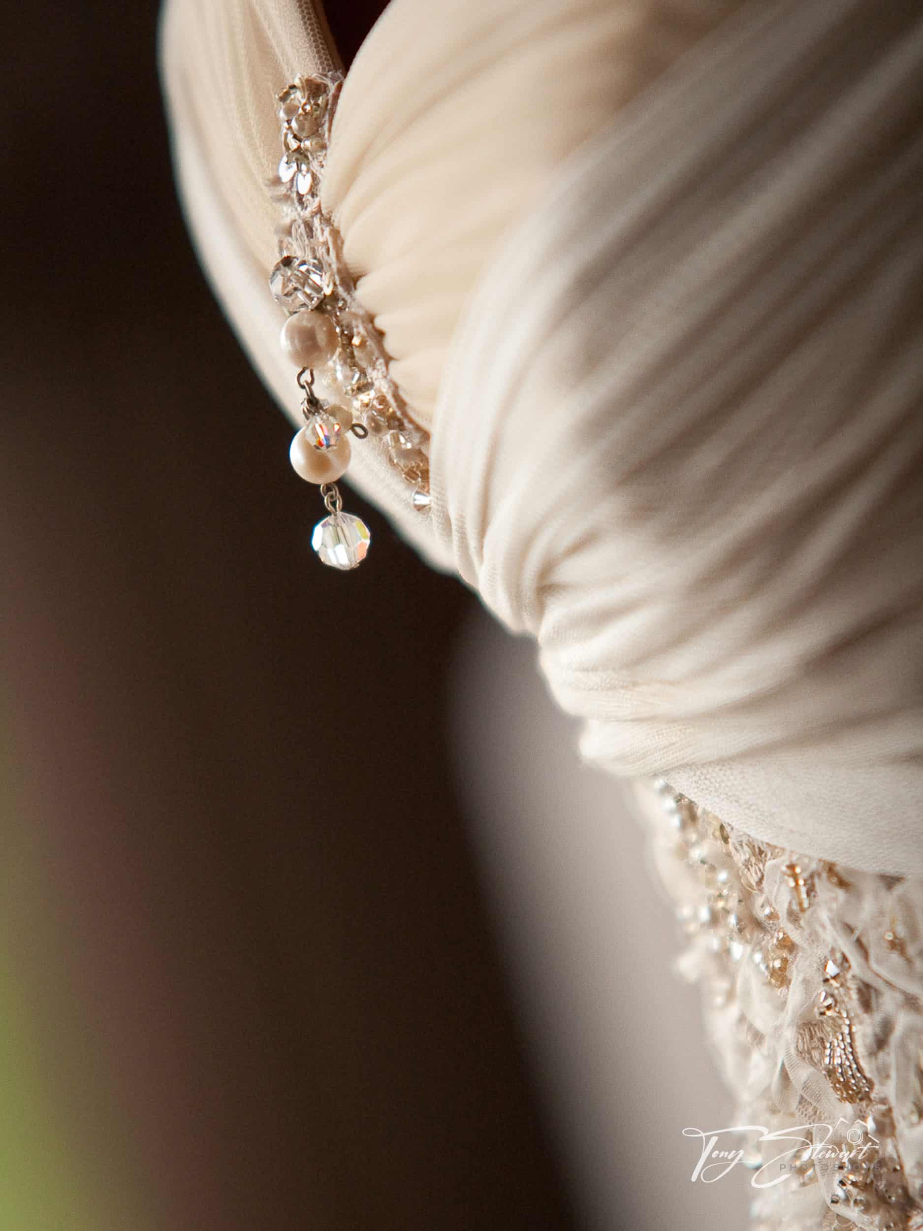 Bridal dress detail showing pearls, intricate fabric folds and lacework.