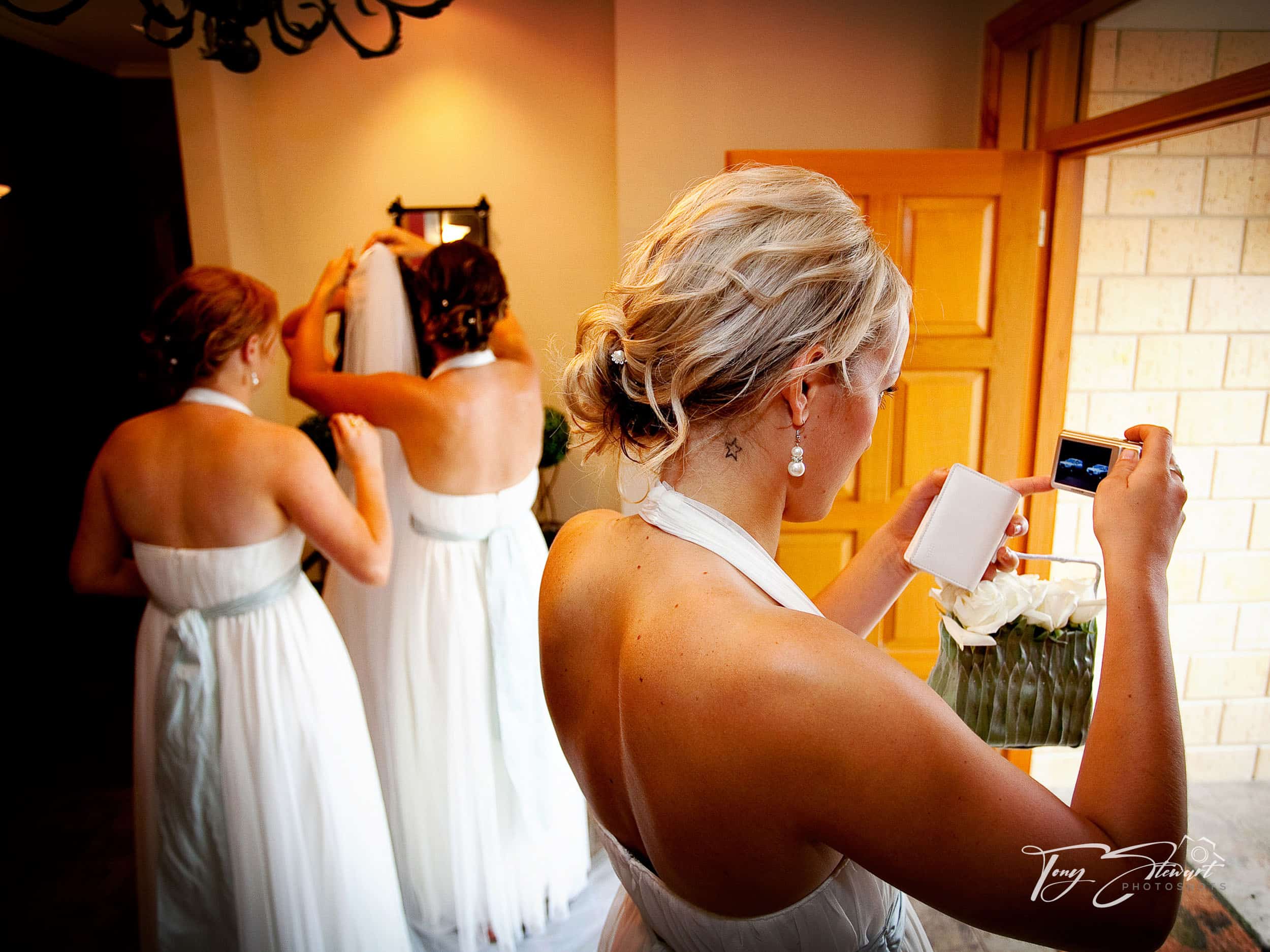A bridesmaid checks earrings, as the bride gets her veil fitted before her wedding ceremony.