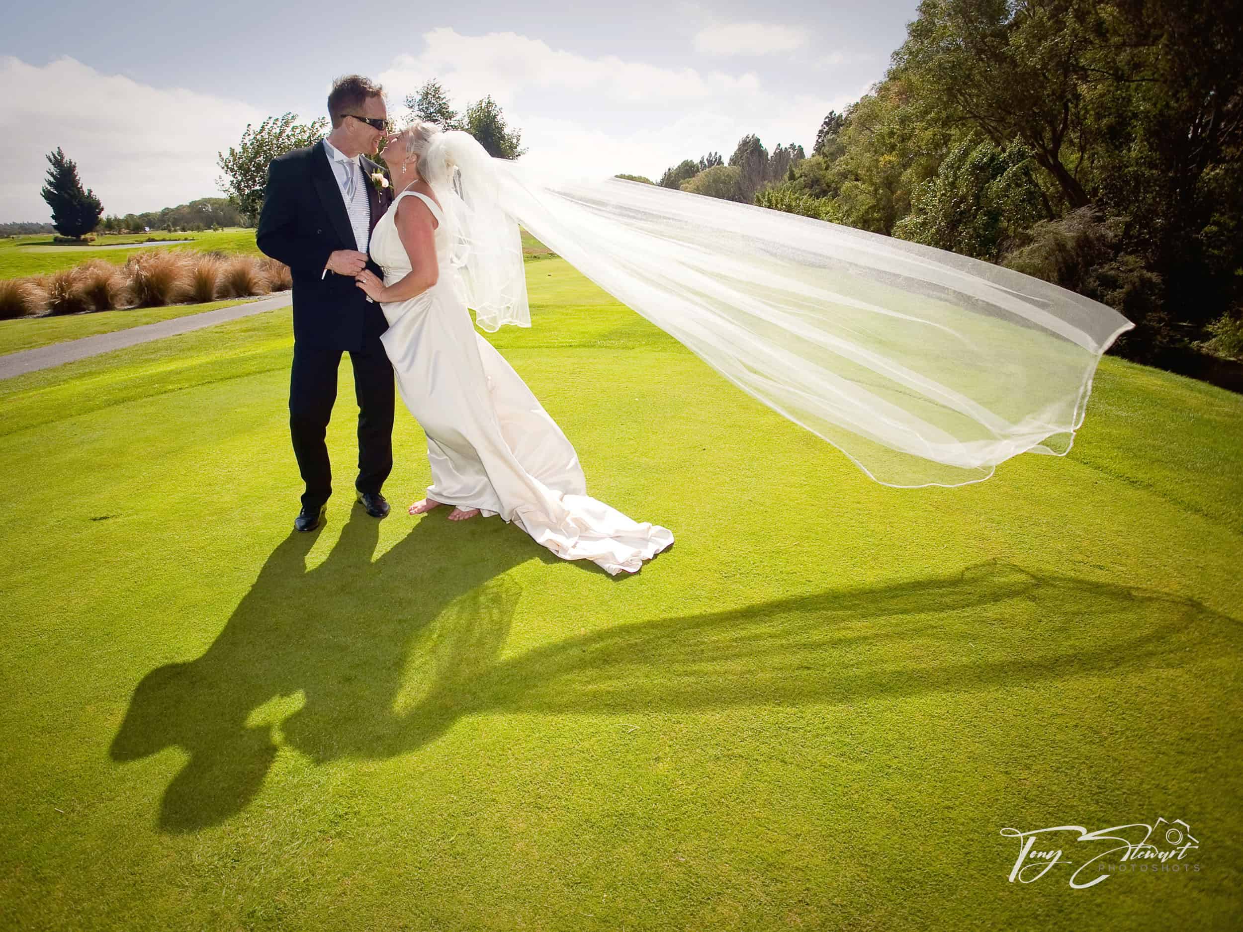 Bridal couple make a funky shadow with veil while kissing on a golf green, Clearwater Resort.