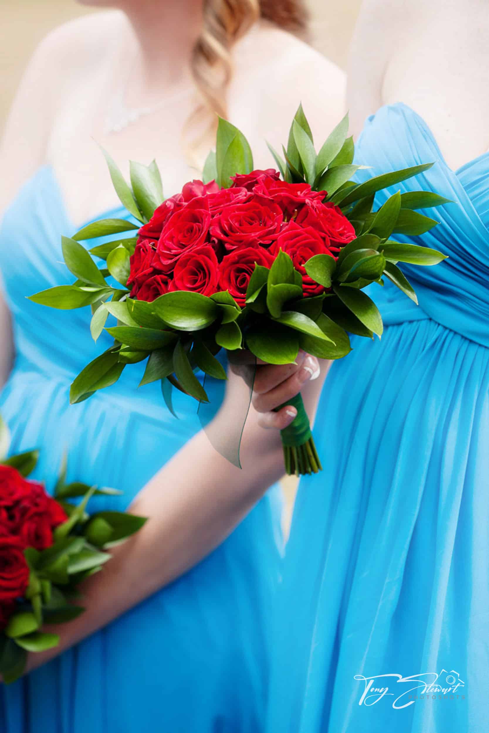 Bright red flowers held against colourful blue bridemaids dresses.