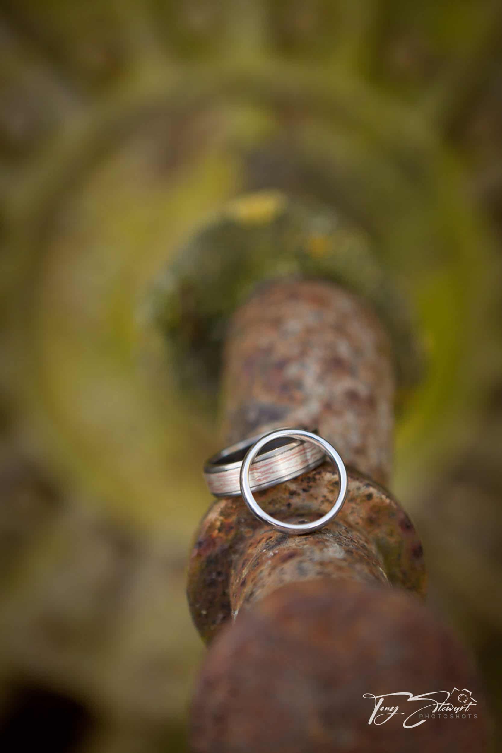 Two wedding rings rest on a rusted pipe.