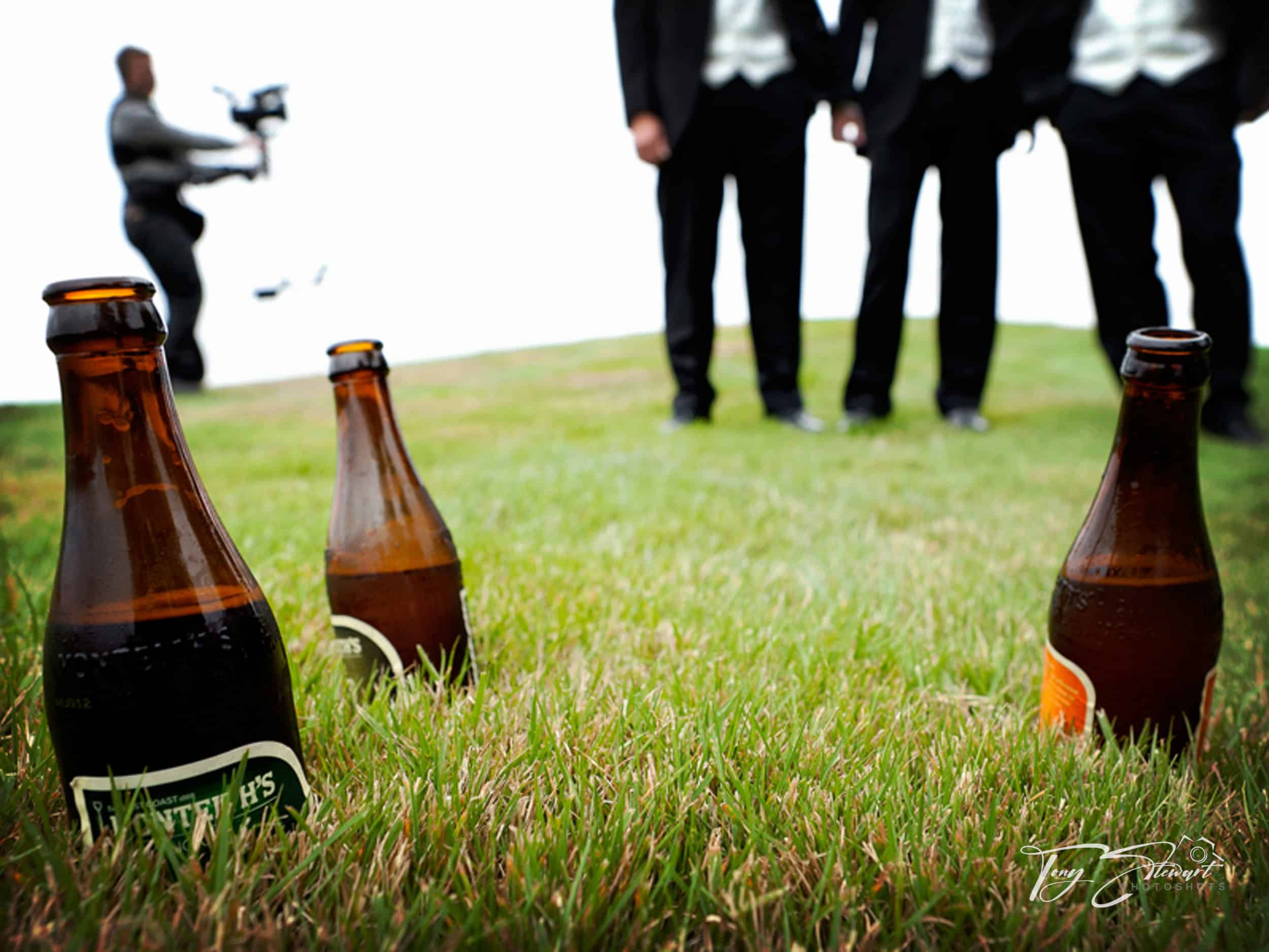 Videographer behind three beer bottles films three groomsmen at Clearwater Resort, Christchurch.