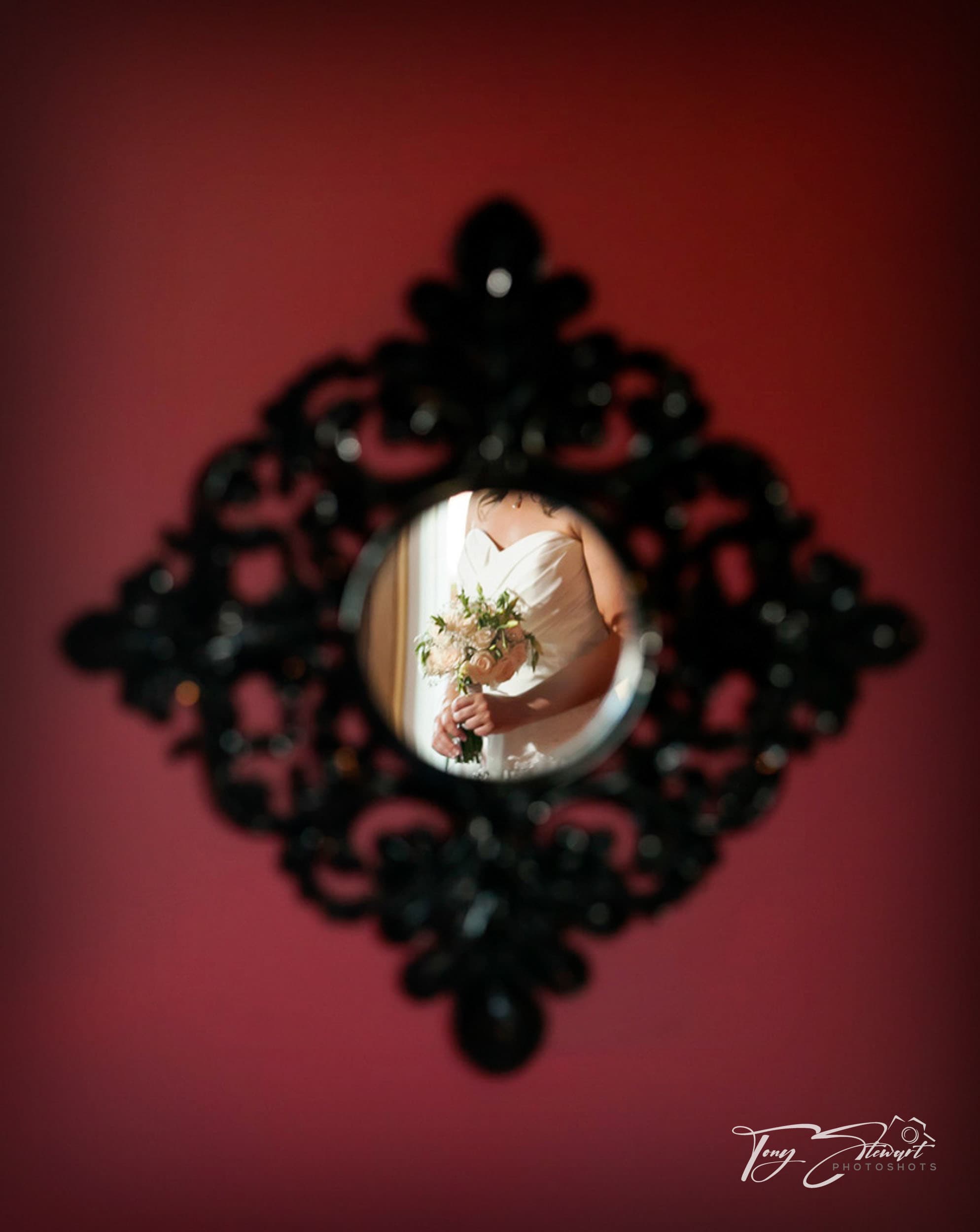 Bride's torso and flowers cropped within the circle of a decorative mirror.
