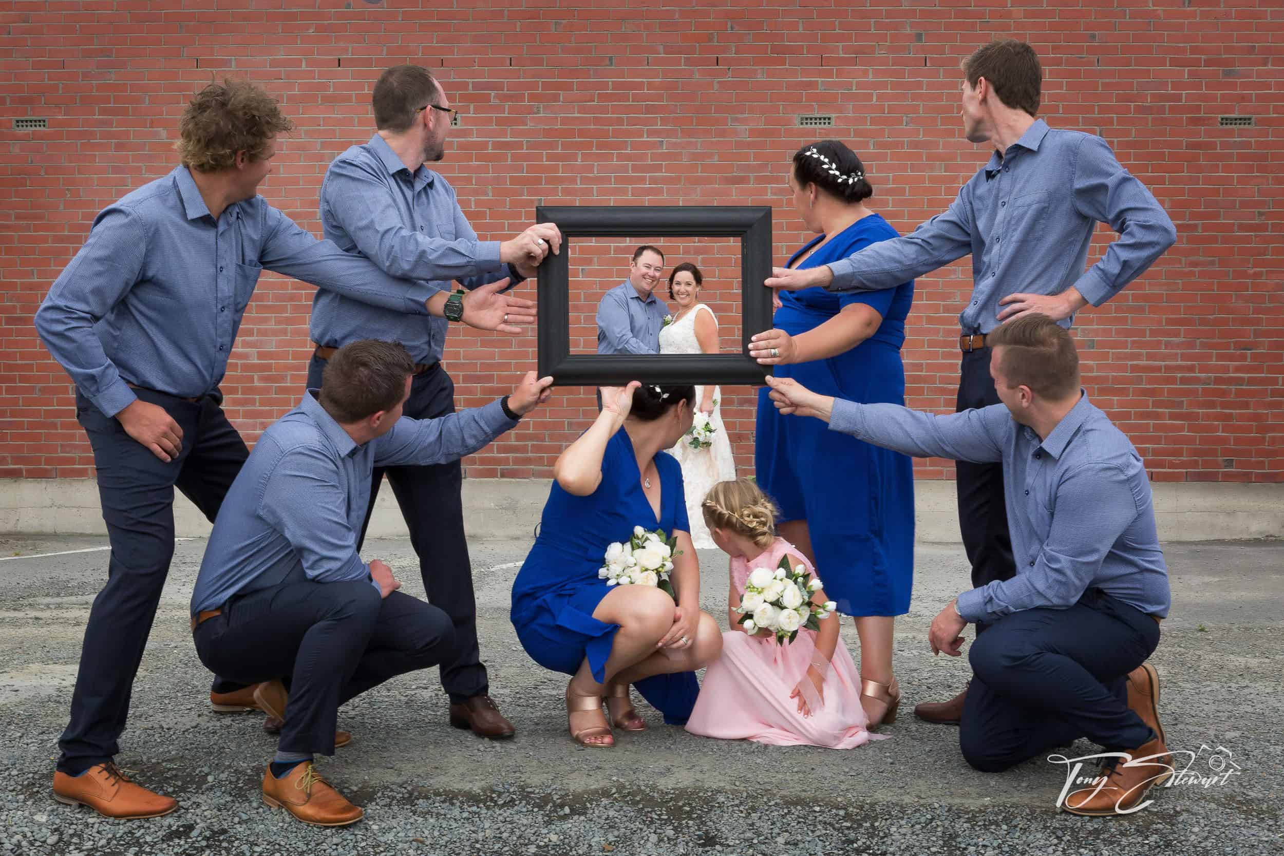Couple pose through a photo frame held up by the rest of their bridal party, in Ashburton.